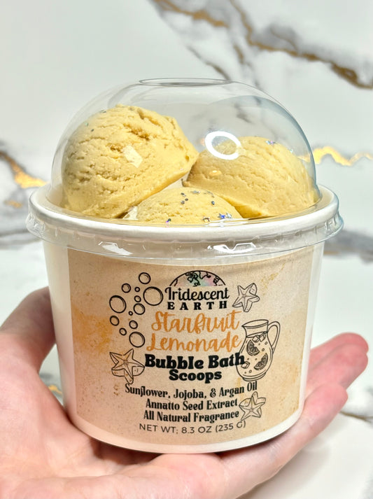 Hand holding a dome top ice cream container of Starfruit lemonade scented bubble bath scoops
