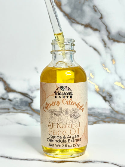 Bottle of Iridescent Earth Calming Calendula All Natural Face Oil with dropper on a marble background