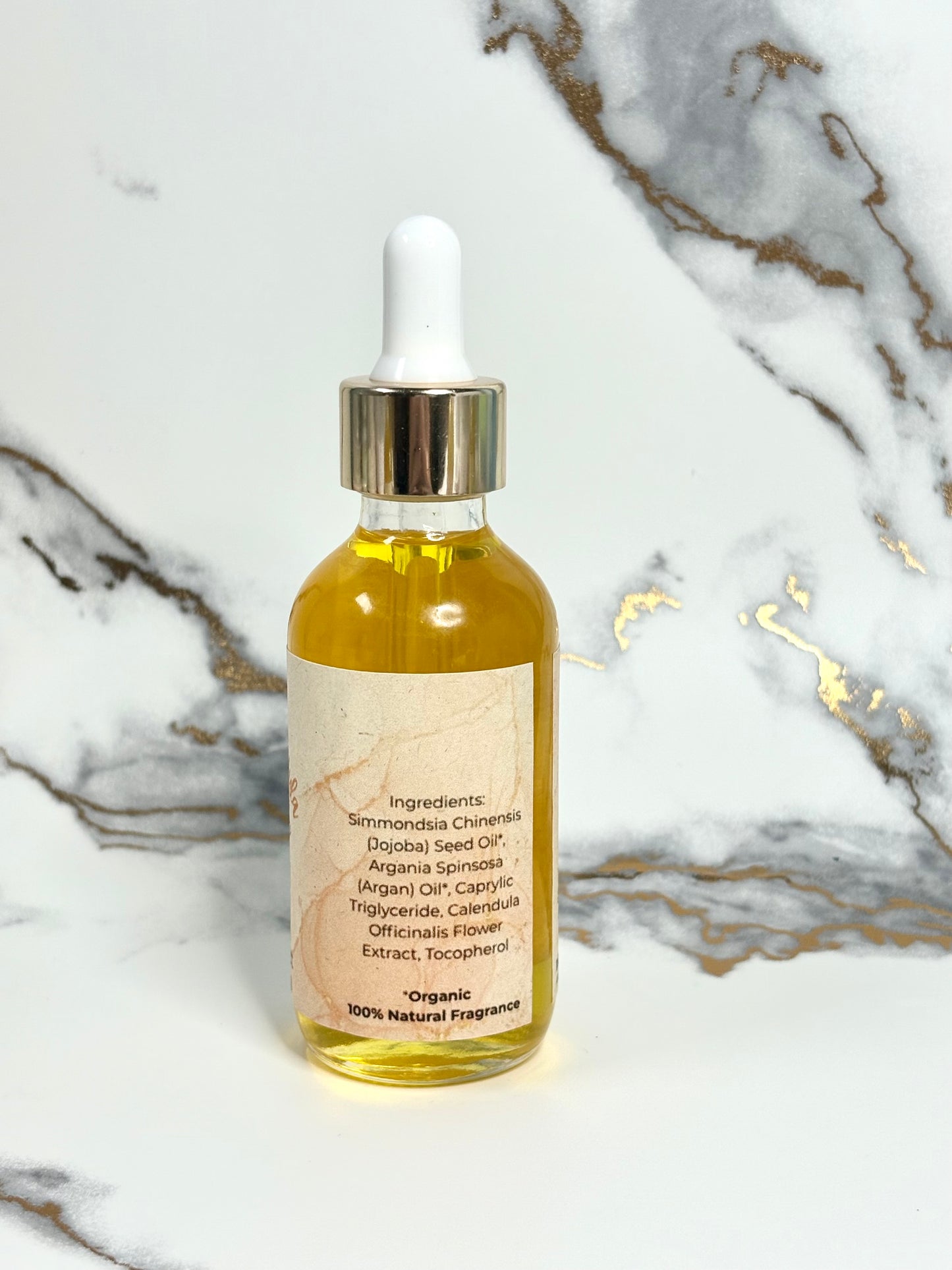 Bottle of calendula, jojoba, and Argan organic face oil with dropper on a marble background