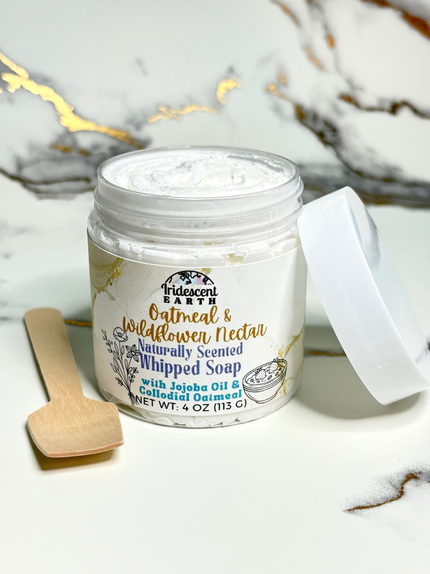 Jar of whipped soap with a wooden spoon on a marble surface