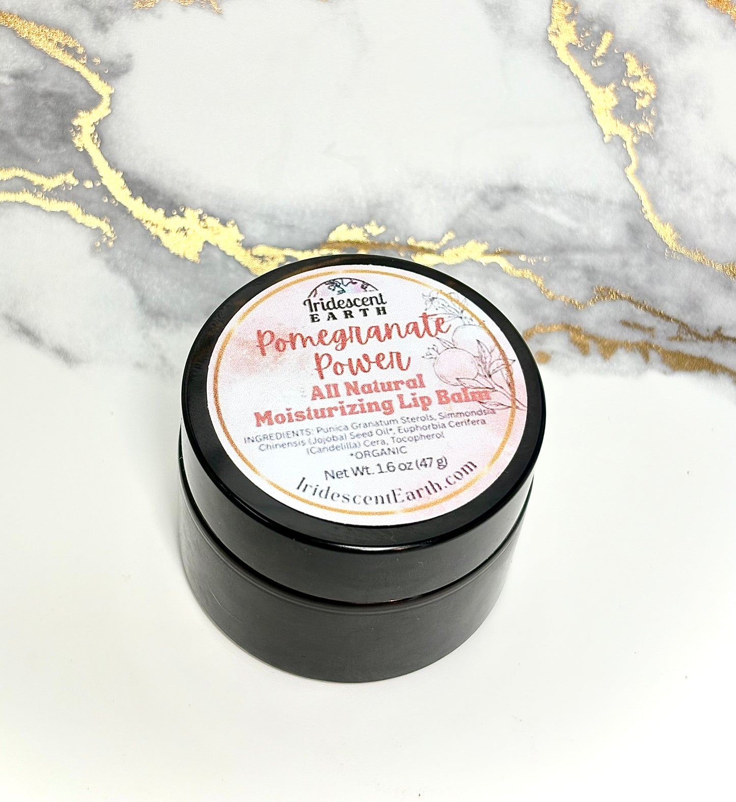 Black container of 'Pomegranate Power' lip balm on a marble background