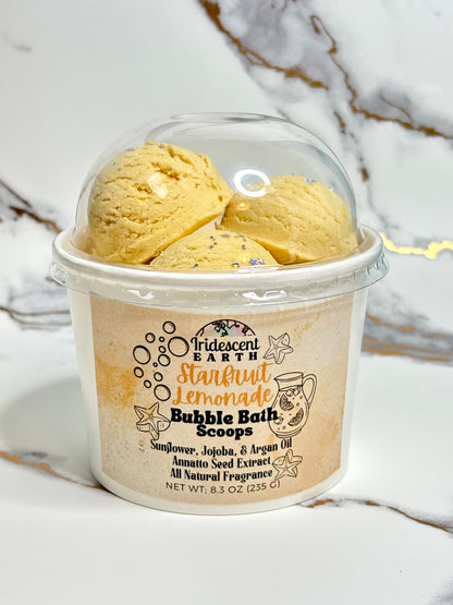 Container of Iridescent Earth Starfruit Lemonade Bubble Bath Scoops on a marble surface