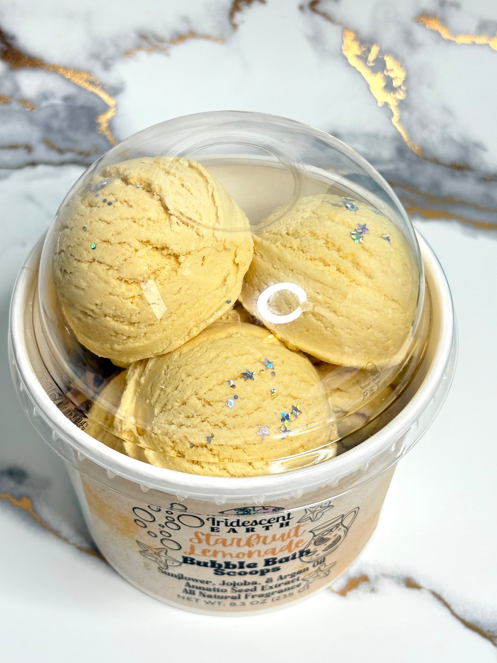 Yellow bubble bath scoops with iridescent biodegradable glitter stars in a container on a marble background
