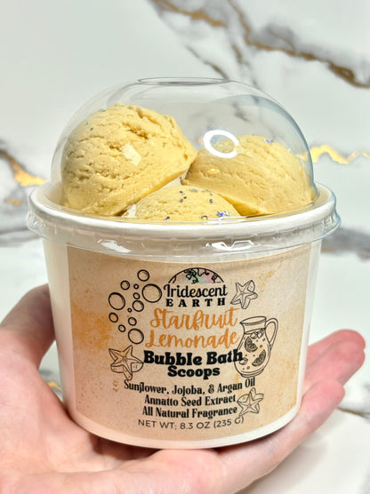 Hand holding a dome top ice cream container of Starfruit lemonade scented bubble bath scoops
